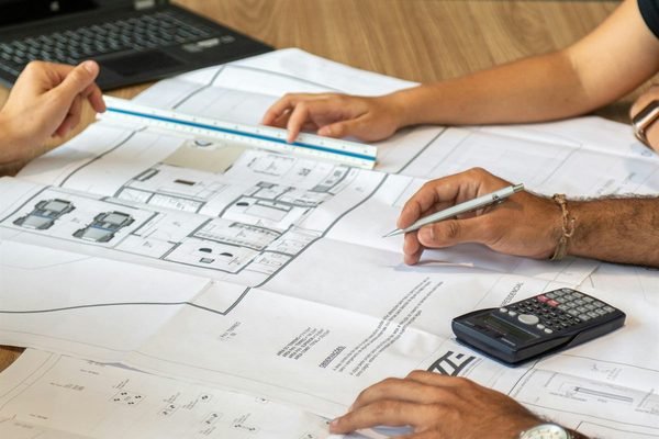 Namo projekto brėžiniai ant stalo, prie jų dirbantys žmonės